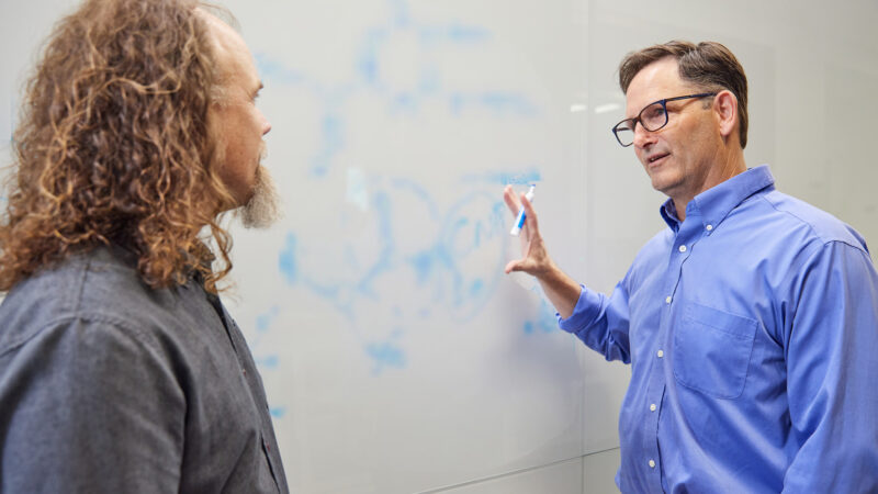 BioMarin scientists Brett Crawford and Dan Wendt talking by a whiteboard with a scientific formula