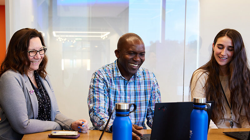 Three employees around a table looking at a computer.